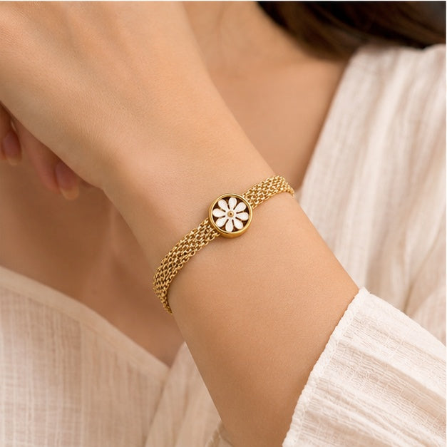 Gold-tone daisy mesh bracelet worn by a woman in a light outfit